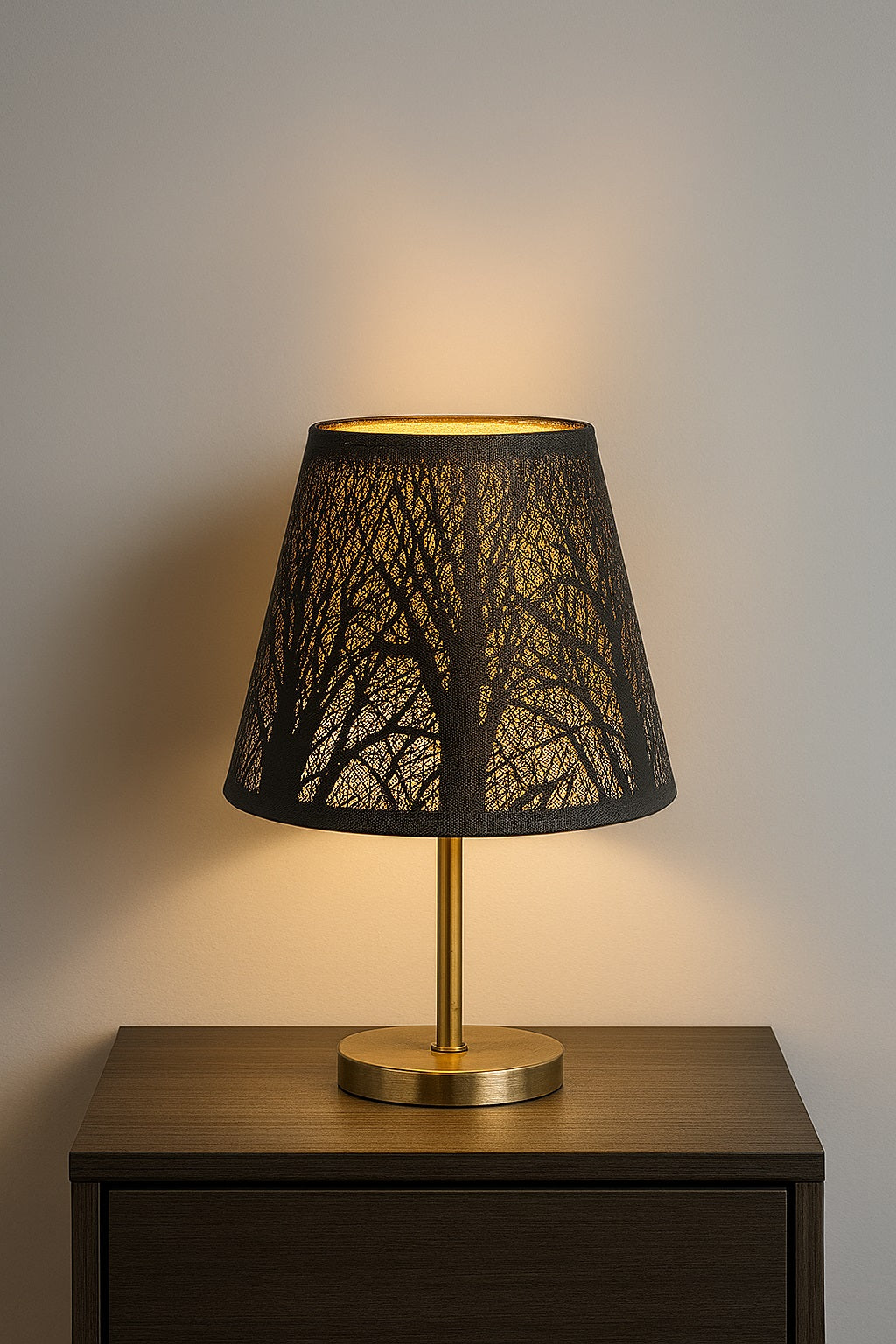 Abat-jour noir et doré ajouré posé sur une lampe de chevet, diffusant une lumière tamisée dans un décor élégant.