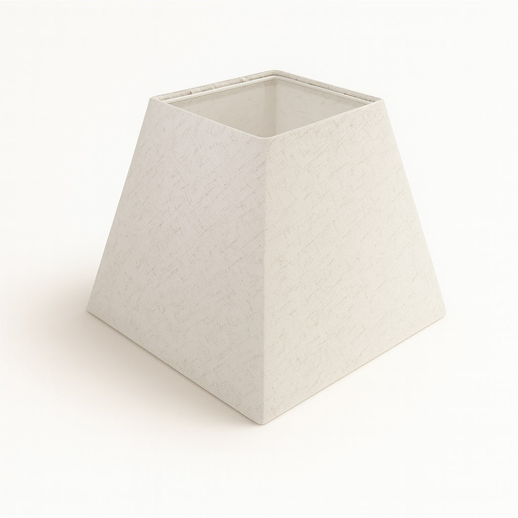 Abat-jour pyramidal en lin blanc avec finition texturée, forme carrée inclinée, posé sur fond clair.