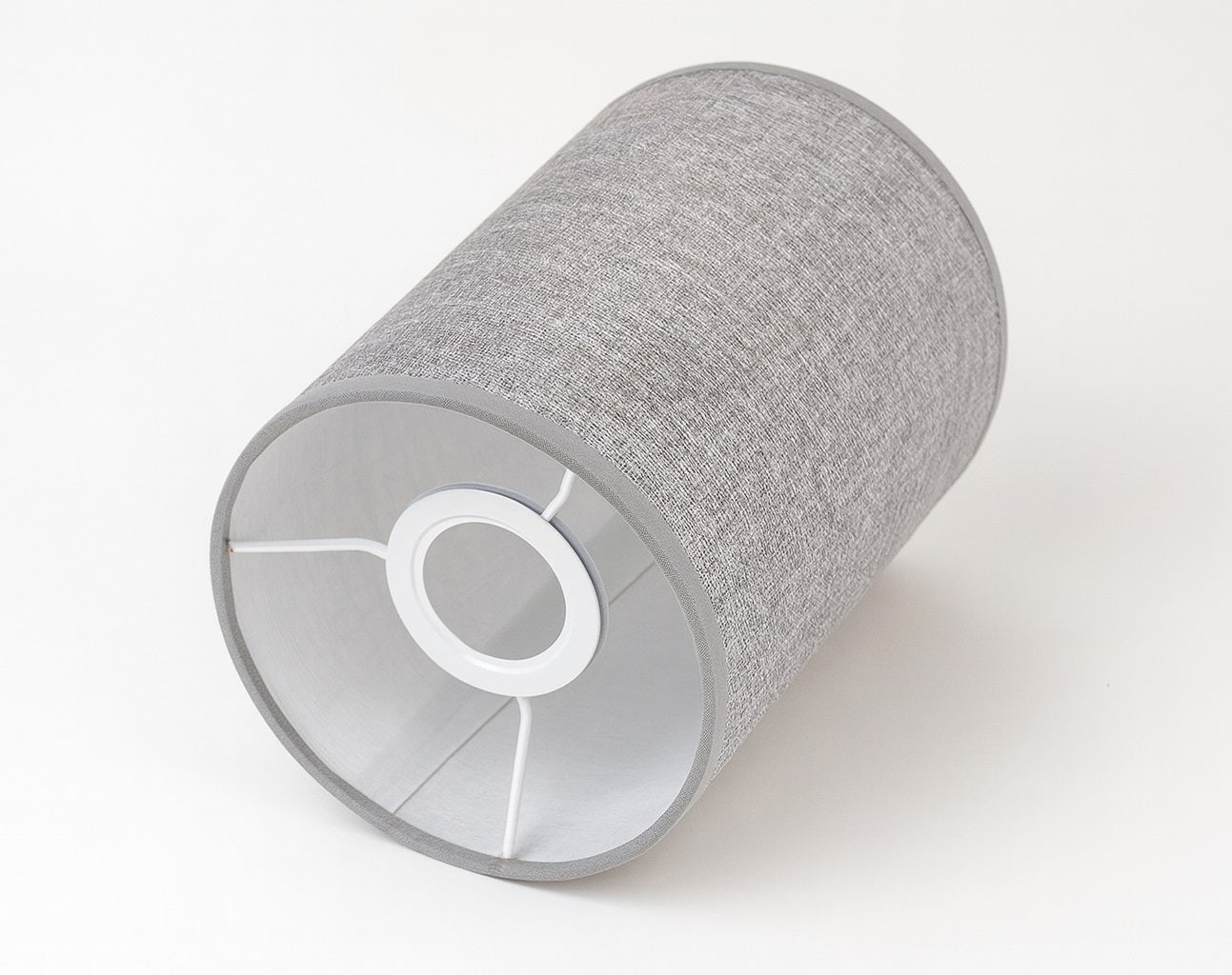 Abat-jour cylindrique en tissu gris posé à l’horizontale sur un fond blanc épuré