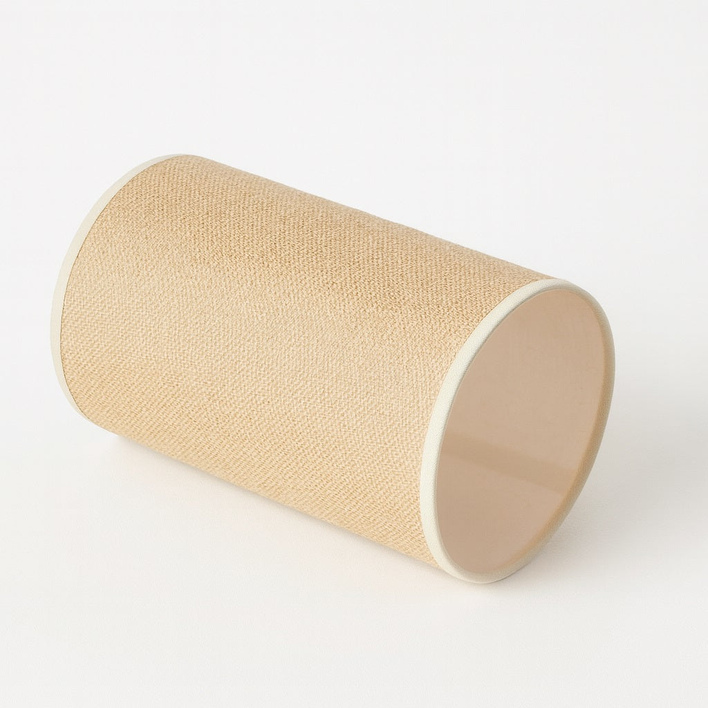 Abat-jour cylindrique en tissu beige posé à l’horizontale sur un fond blanc épuré