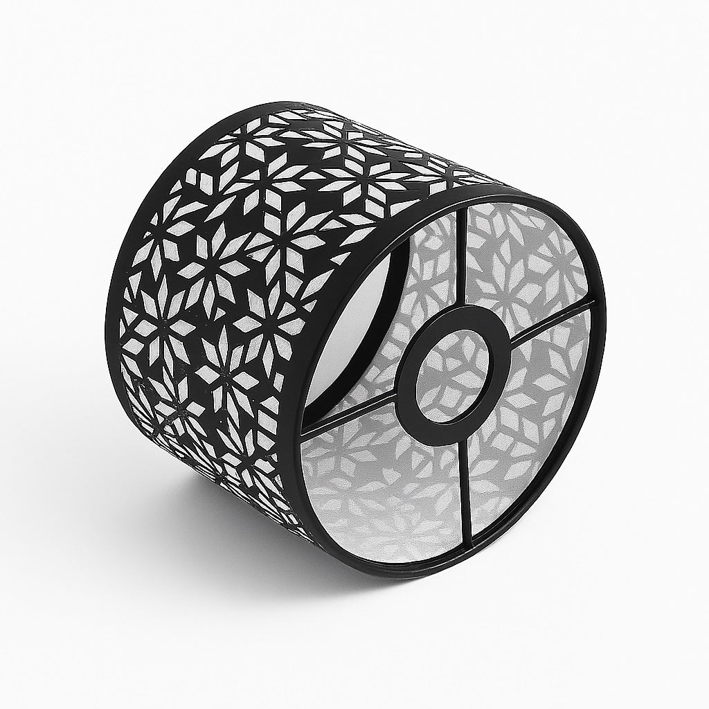 Abat-jour cylindrique en métal noir à motif étoile, posé de biais sur fond blanc – design ajouré et structure à 4 branches.