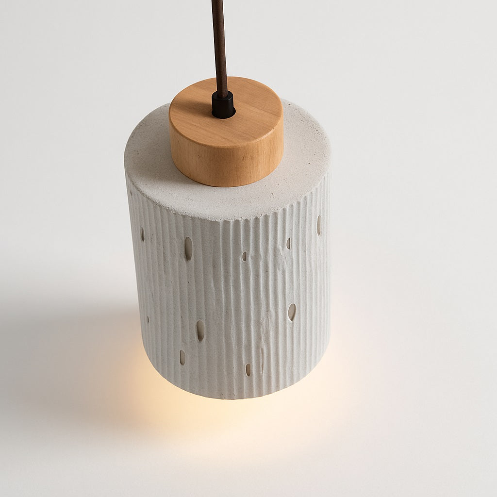 Lampe suspension Arboza en ciment et bois clair, forme cylindrique avec relief vertical et perforations design.
