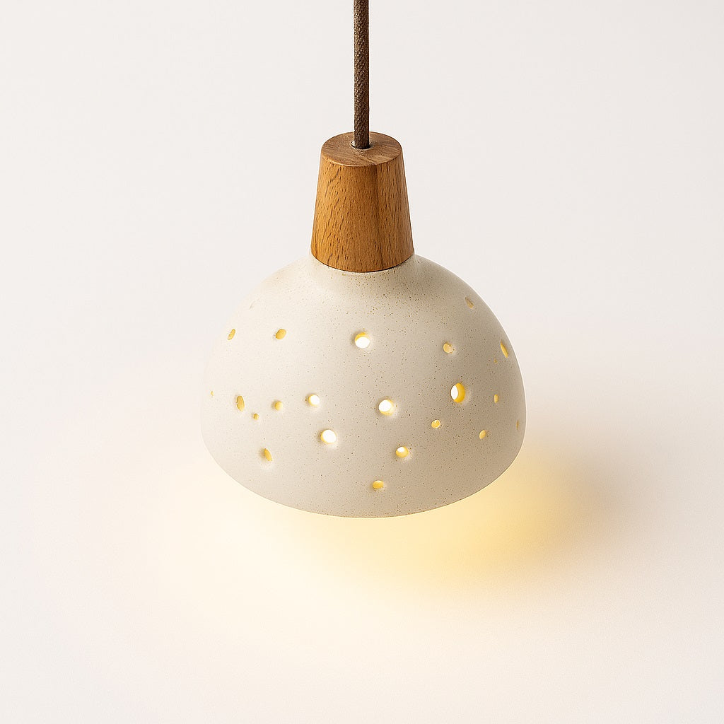 Lampe suspension en ciment perforé et bois clair, design organique diffusant une lumière chaleureuse vers le bas.