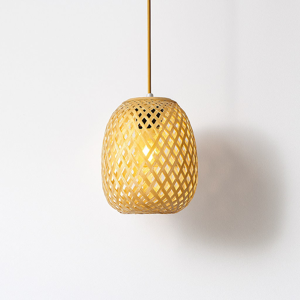 Suspension en rotin naturel tressé, forme ovale, lumière douce projetée sur mur blanc, design artisanal épuré.