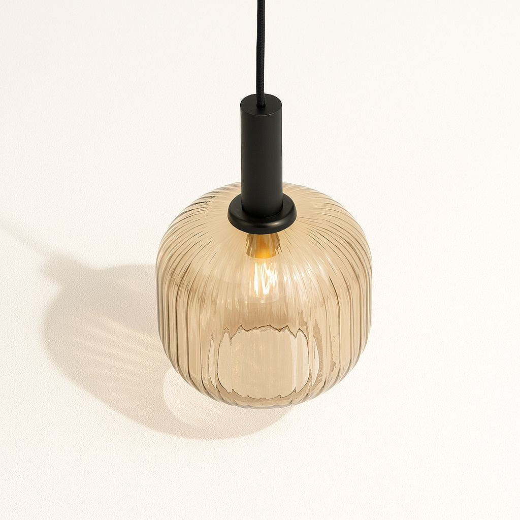 Abat-jour en verre nervuré ambre vu de dessus, avec douille noire mate et lumière chaleureuse projetée au mur.