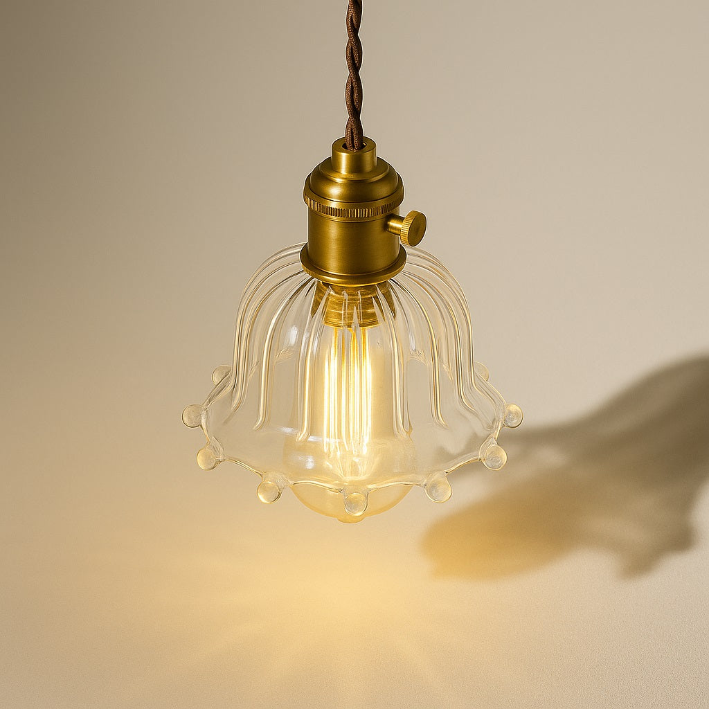 Lampe suspendue vue du dessus à 45°, abat-jour en verre nervuré avec finitions perlées, douille laiton, lumière chaleureuse.