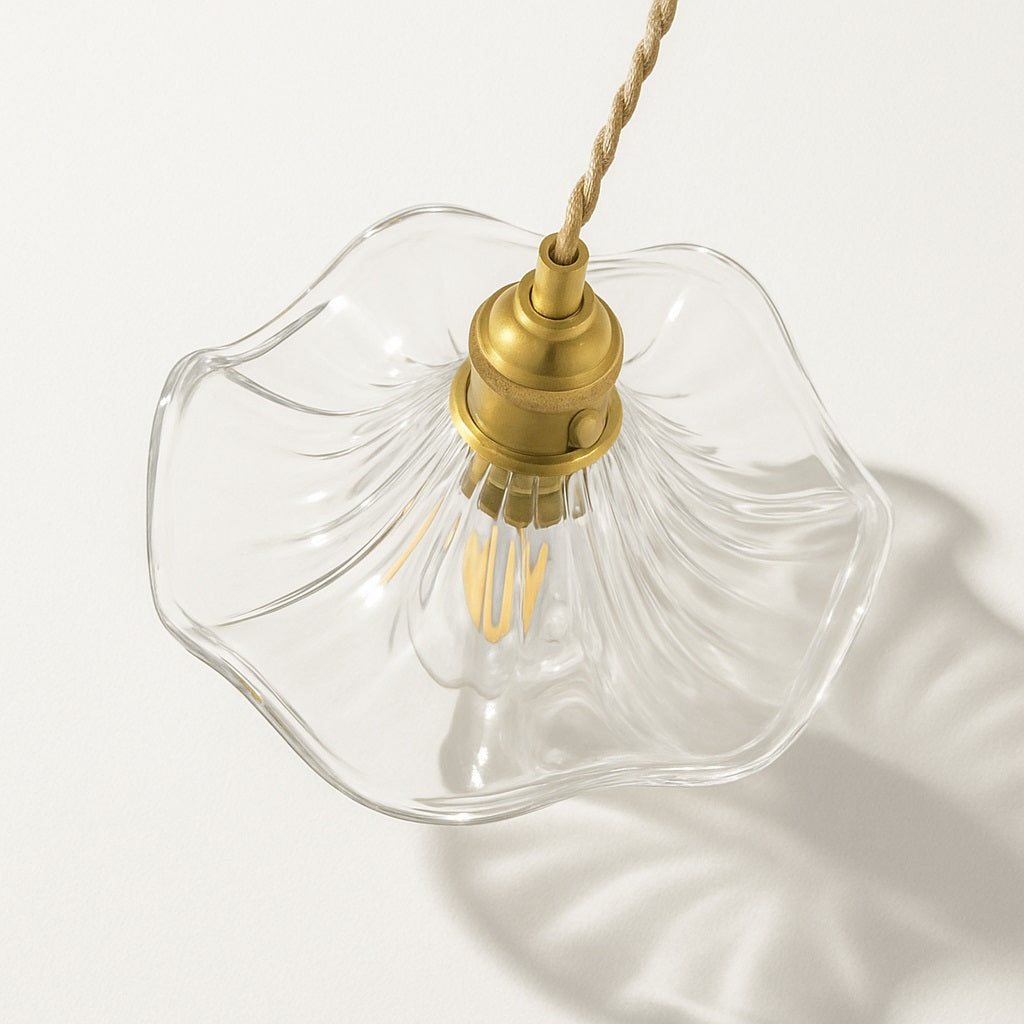 Vue plongeante sur une suspension en verre ondulé transparent avec douille dorée et ampoule LED décorative.