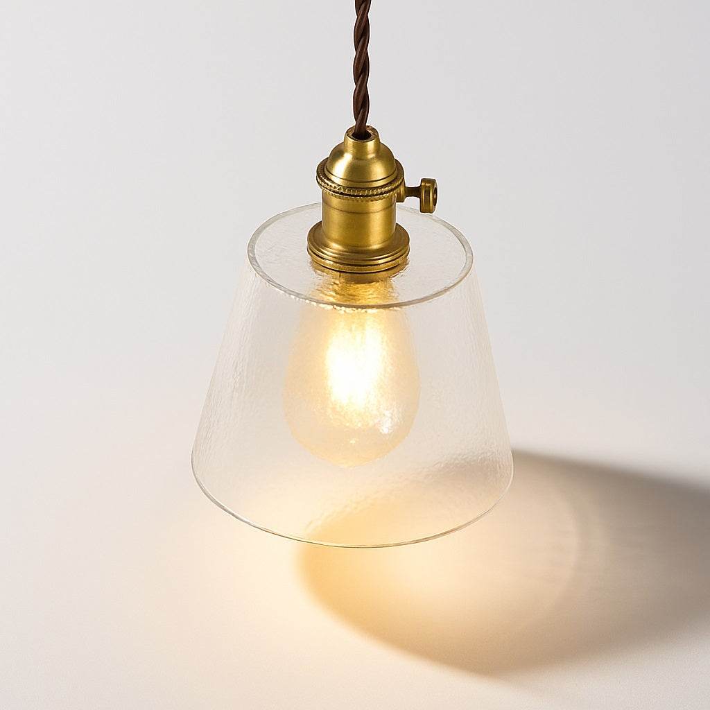 Lampe suspendue vue du dessus à 45°, abat-jour conique en verre transparent et douille en laiton, lumière chaude.