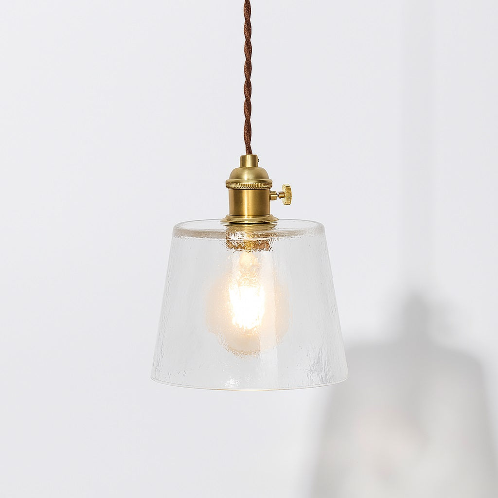 Suspension en verre transparent texturé avec douille laiton doré et cordon textile marron, style vintage.