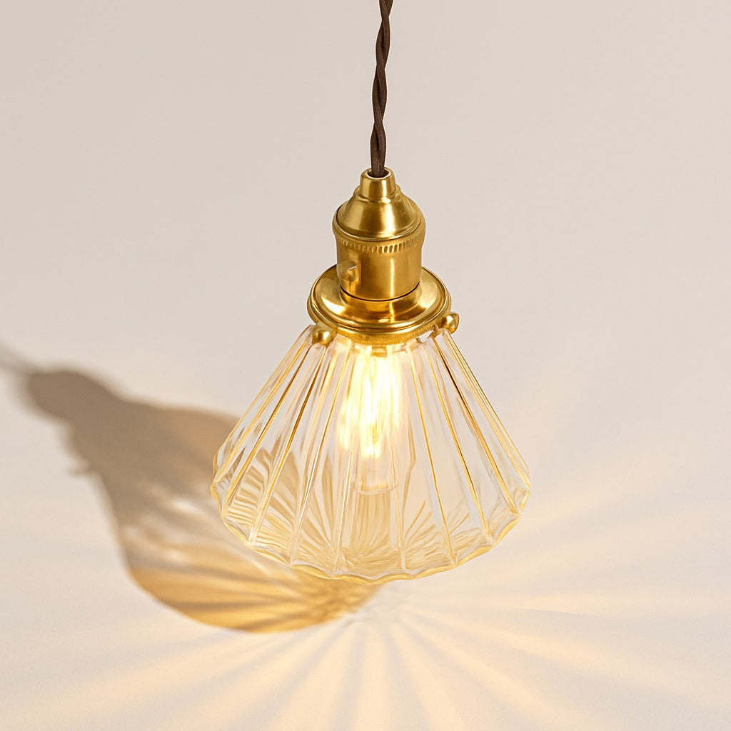 Abat-jour suspension en verre facetté diffusant une lumière chaleureuse sur fond neutre, vue plongeante design.
