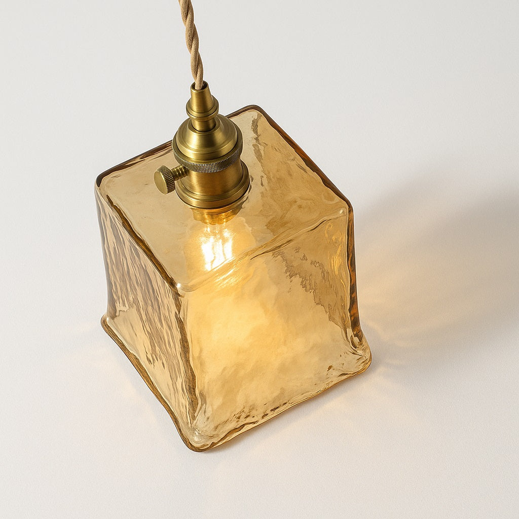 Abat-jour suspension en verre carré nervuré ambre, vue en angle avec douille laiton et lumière chaude diffuse.