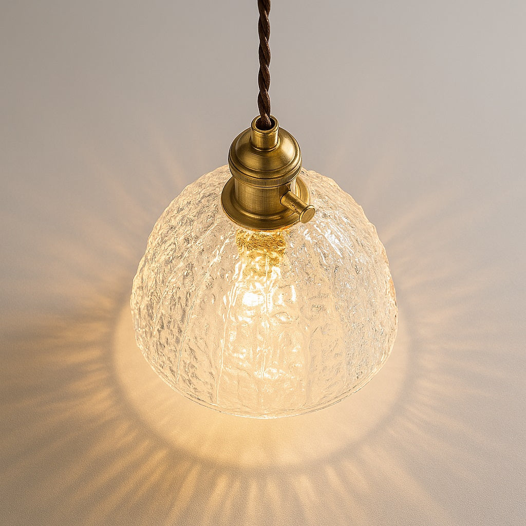 Lampe suspendue vue du dessus à 45°, abat-jour en verre martelé diffusant une lumière chaleureuse, douille laiton.