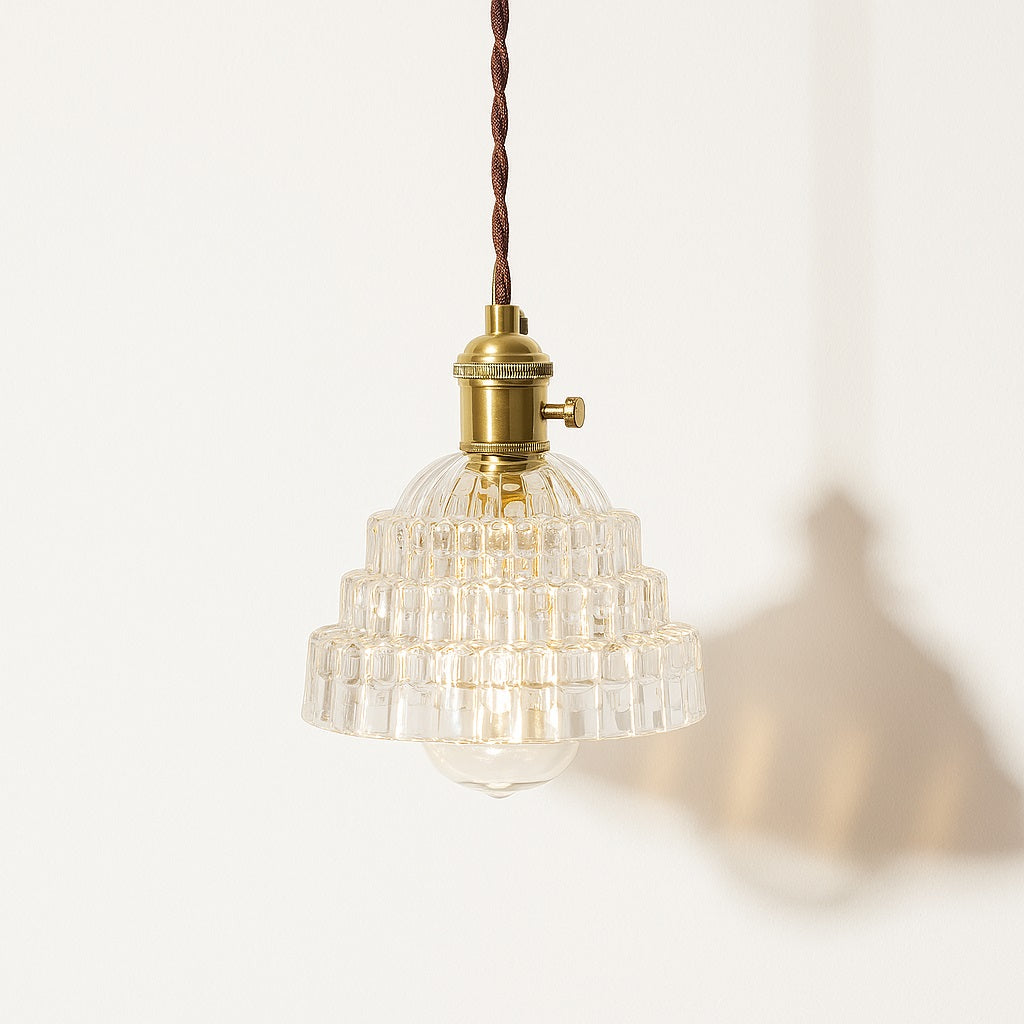 Suspension en verre transparent à étages géométriques, douille laiton doré, lumière douce et structurée.