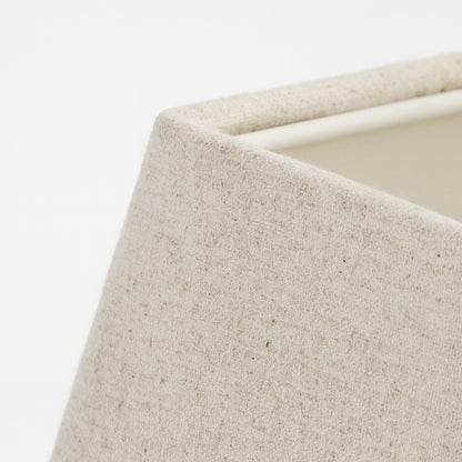 Gros plan sur la texture en lin naturel d’un abat-jour pyramide blanc pour lampe moderne et épurée.