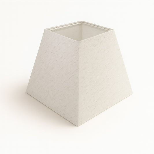 Abat-jour pyramidal en lin blanc avec finition texturée, forme carrée inclinée, posé sur fond clair.