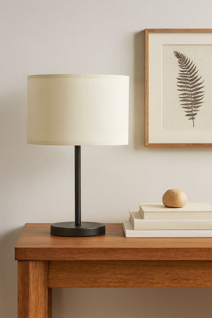 Abat-jour tambour en lin blanc, posé sur lampe moderne noire, déco sobre et élégante avec cadre botanique.