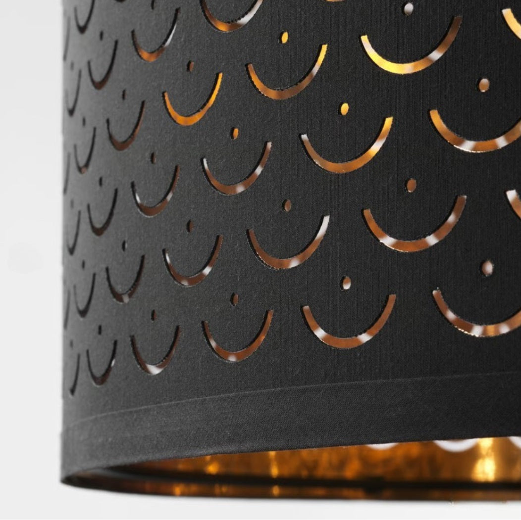 Gros plan sur abat-jour tambour noir et doré, motifs ajourés lumineux pour suspension ou lampadaire chic.