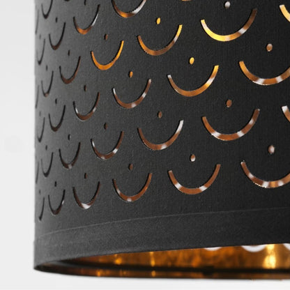 Gros plan sur abat-jour tambour noir et doré, motifs ajourés lumineux pour suspension ou lampadaire chic.