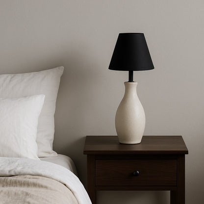 Abat-jour conique noir sur lampe de chevet, éclairage moderne et minimaliste pour une chambre élégante.