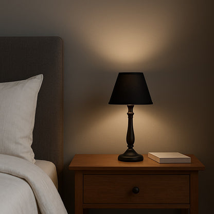 Abat-jour lampe de chevet noir allumé, abat-jour conique diffusant une lumière douce en ambiance nocturne.