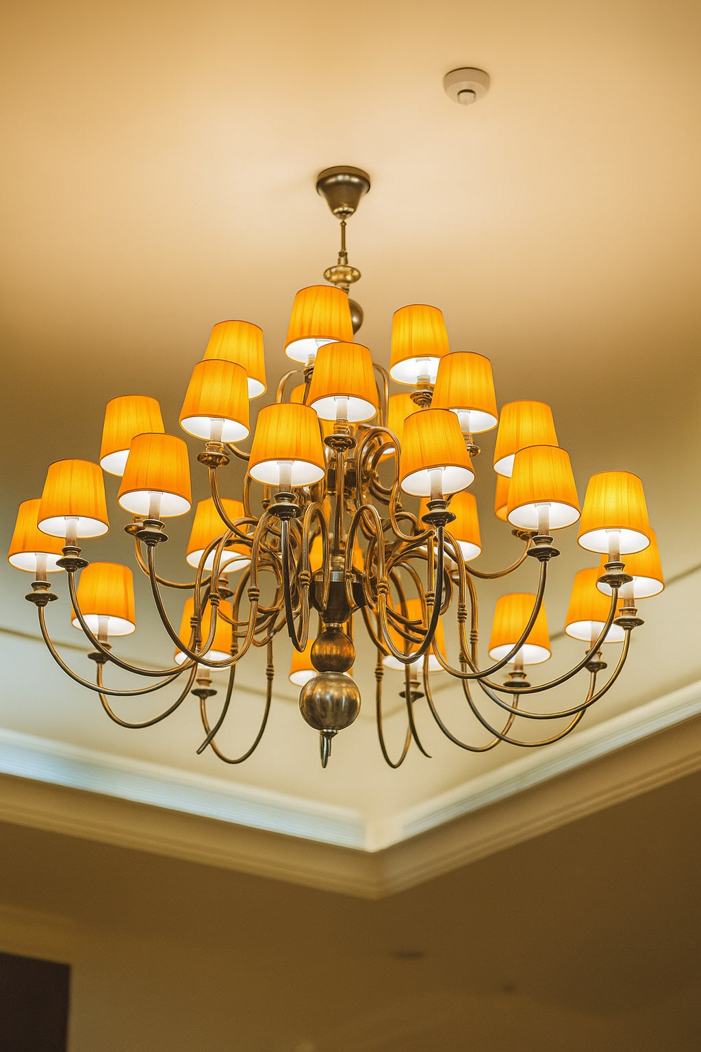 Grand lustre design avec 24 abat-jour orange allumés, suspendu au plafond d’un intérieur élégant – éclairage décoratif haut de gamme.