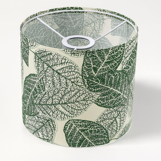 Abat-jour cylindrique en tissu à motif feuillage vert sur fond beige, vue de dessus avec structure métallique intérieure blanche.