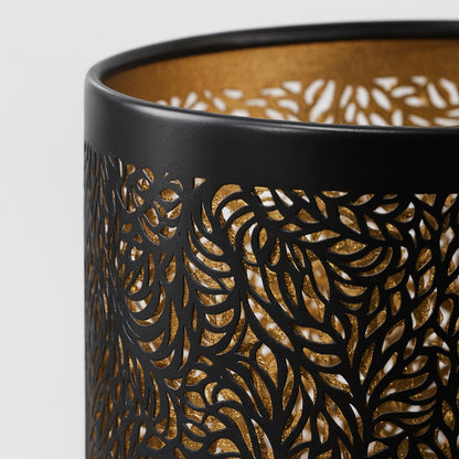 Détail d’un abat-jour en métal noir ajouré avec intérieur doré, motif floral finement découpé, effet lumineux élégant.