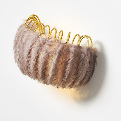 Vue en angle d'une applique plume brune sur structure dorée, lumière tamisée élégante.