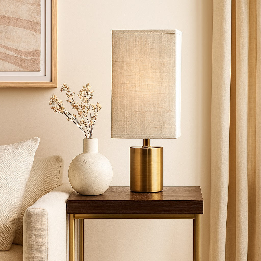 Abat-jour pour lampe rectangulaire en lin clair sur pied doré, posé sur une table d’appoint élégante.