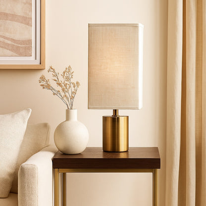 Abat-jour pour lampe rectangulaire en lin clair sur pied doré, posé sur une table d’appoint élégante.