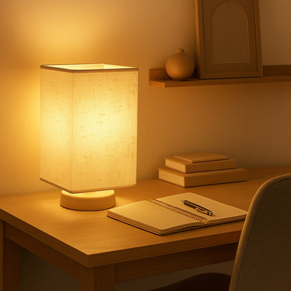 Abat-jour pour lampe de bureau en tissu beige diffusant une lumière chaude sur un bureau en bois clair.