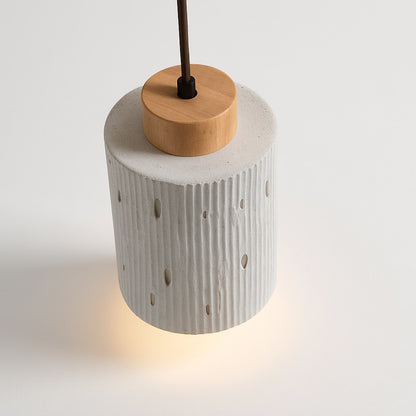 Lampe suspension Arboza en ciment et bois clair, forme cylindrique avec relief vertical et perforations design.