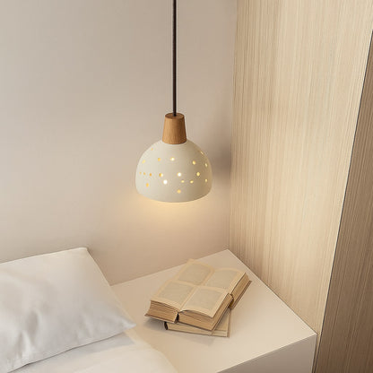 Suspension en ciment perforé au-dessus d’une table de chevet, lumière douce et design naturel pour chambre moderne.