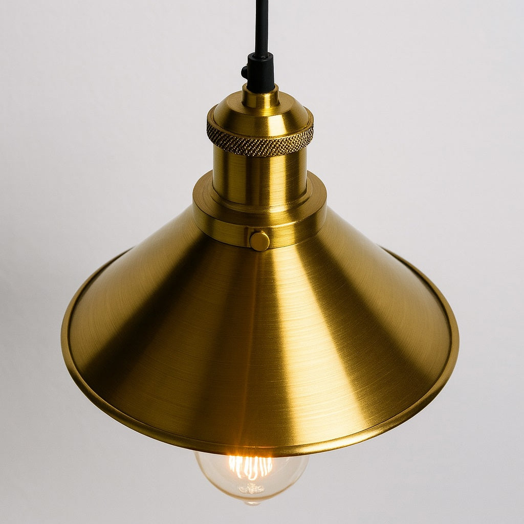 Gros plan sur un abat-jour métal en suspension doré, finition brossée et ampoule rétro visible.