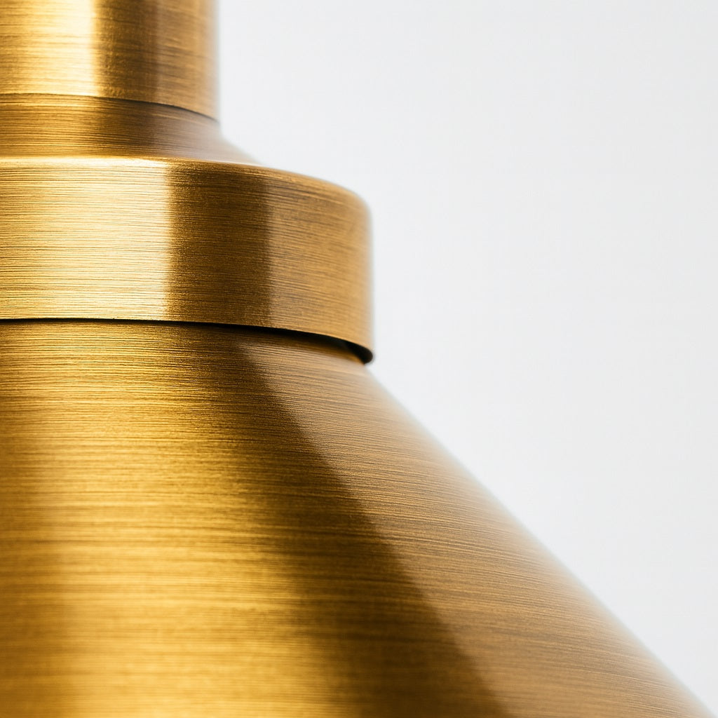 Zoom sur la texture brossée d’un abat-jour métal en suspension doré, finition premium brillante.