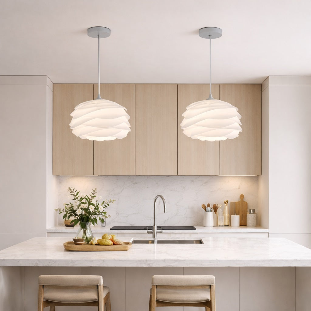Abat-jour suspension blanc au design sculptural, installé au-dessus d’un îlot de cuisine moderne et épuré