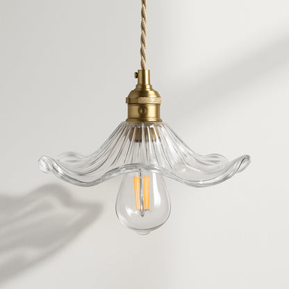 Suspension florale en verre transparent, douille laiton et ampoule LED, ombre portée au mur.