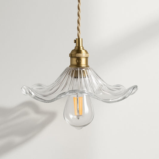 Suspension florale en verre transparent, douille laiton et ampoule LED, ombre portée au mur.