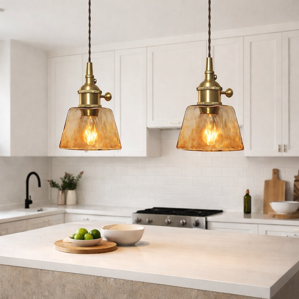 Abat-jour suspension en verre ambré au style vintage, installé au-dessus d’un îlot de cuisine moderne et lumineux