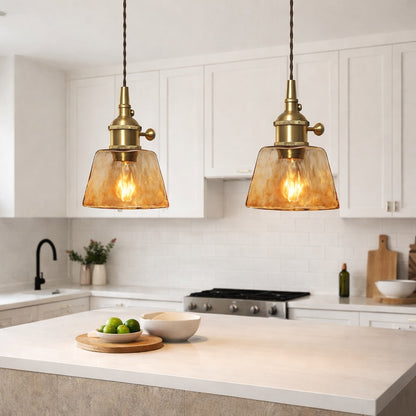 Abat-jour suspension en verre ambré au style vintage, installé au-dessus d’un îlot de cuisine moderne et lumineux