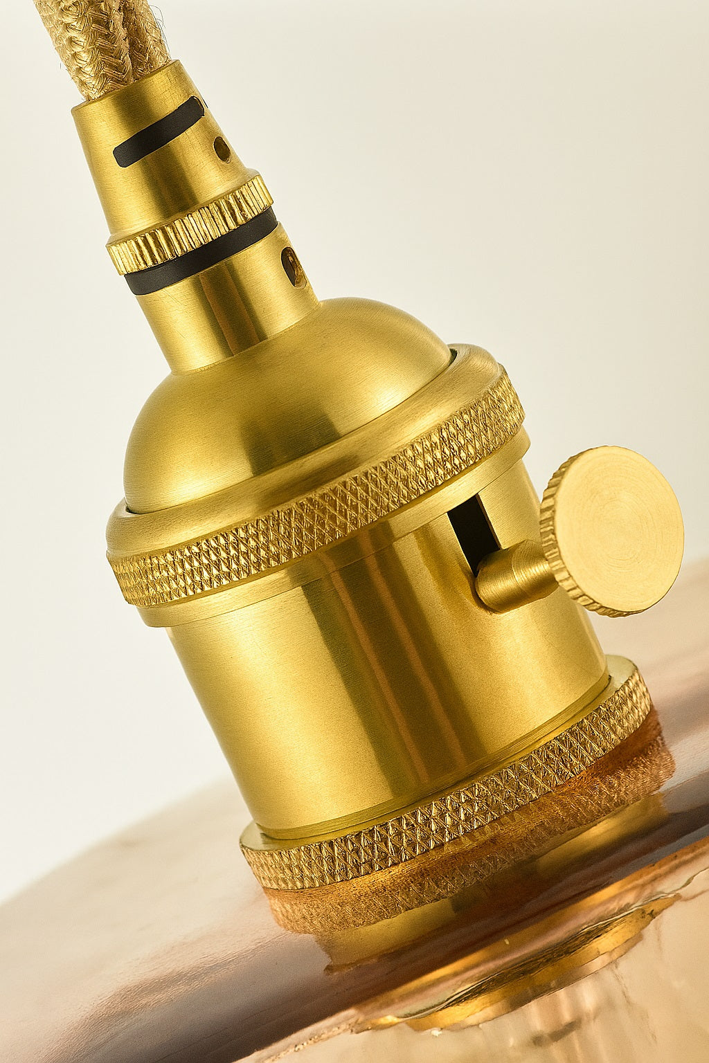 Gros plan sur douille E27 en laiton doré pour suspension design avec abat-jour en verre soufflé.