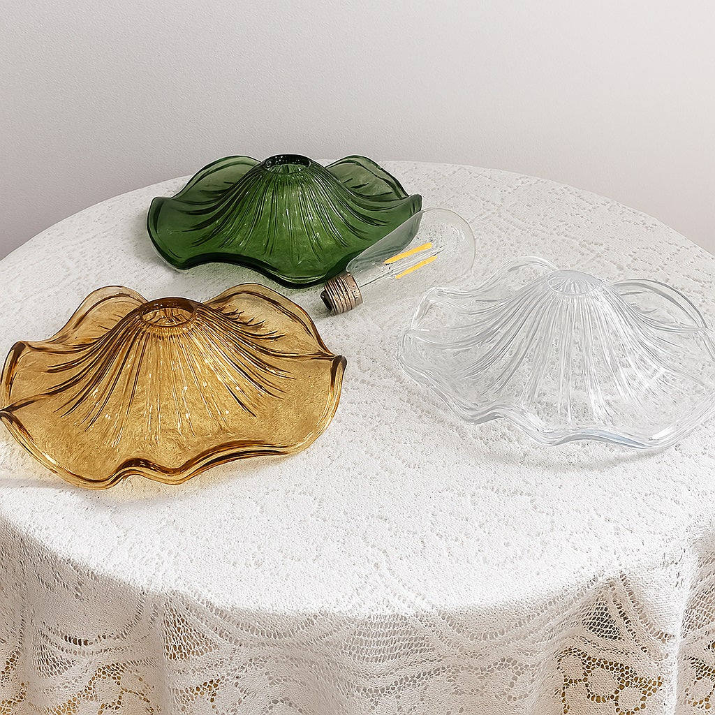 Trois abat-jour en verre soufflé posés sur table en dentelle : vert, ambre et transparent, pour suspensions décoratives vintage.
