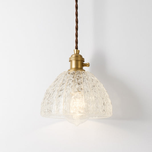 Suspension en verre martelé transparent, forme dôme, douille laiton doré, lumière douce et design brut.