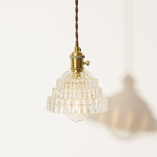 Suspension en verre transparent à étages géométriques, douille laiton doré, lumière douce et structurée.