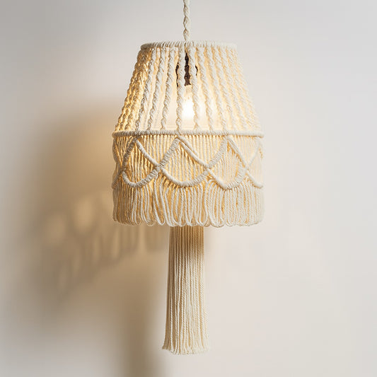 Suspension en coton blanc torsadé avec pompon central, tressage ajouré et lumière douce projetée au mur.