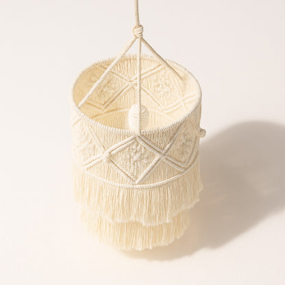 Abat-jour en coton blanc macramé, tressage en losange et franges superposées, vu de dessus sur fond blanc lumineux.
