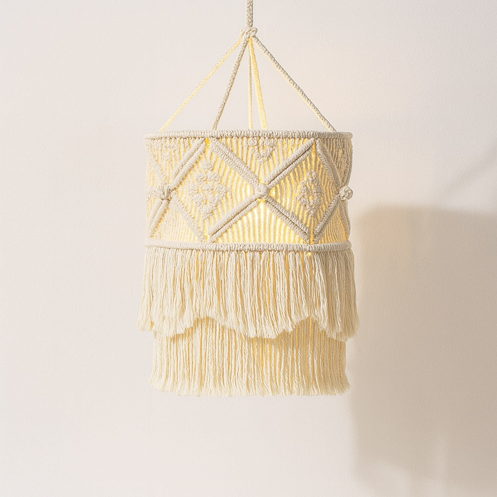Suspension en coton blanc à franges, abat-jour bohème avec tissage géométrique et lumière douce sur fond neutre.