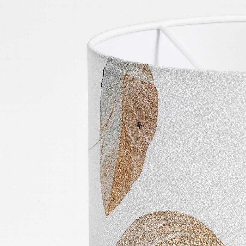 Détail d’un abat-jour blanc en tissu imprimé de feuilles beiges, texture naturelle et finition soignée.